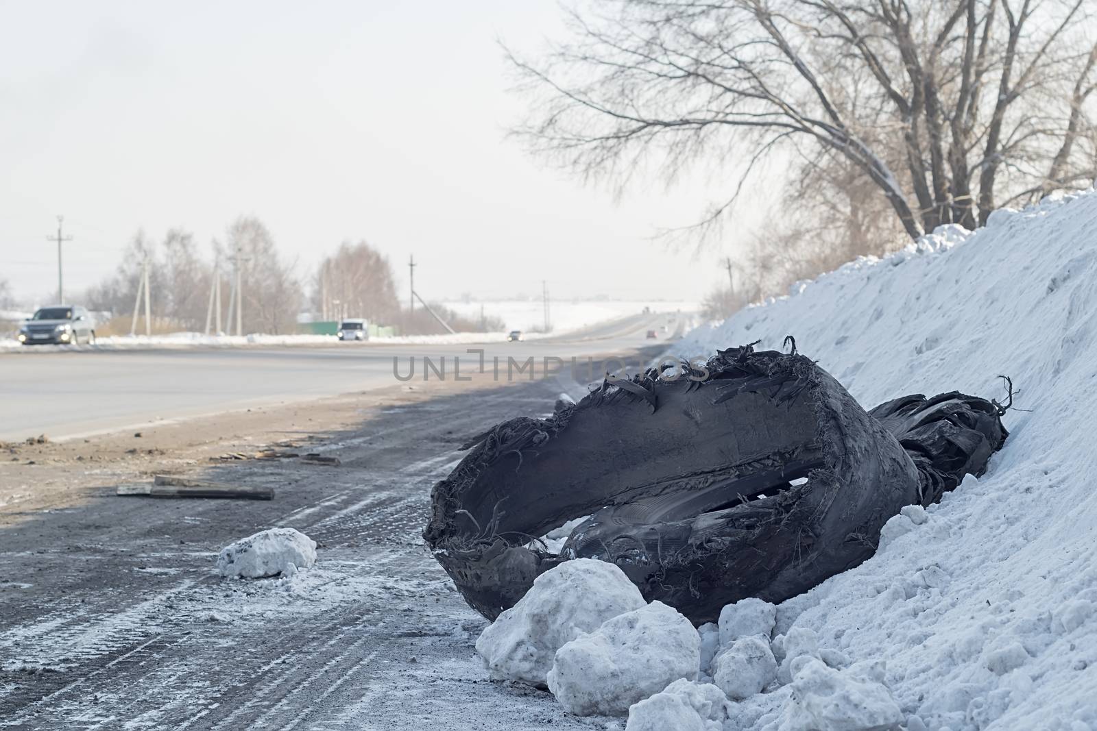 a torn car tire from a truck lies in the snow on the side of the road by jk3030