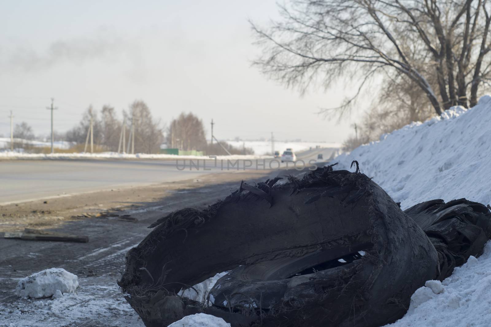 a torn car tire from a truck lies in the snow on the side of the road by jk3030