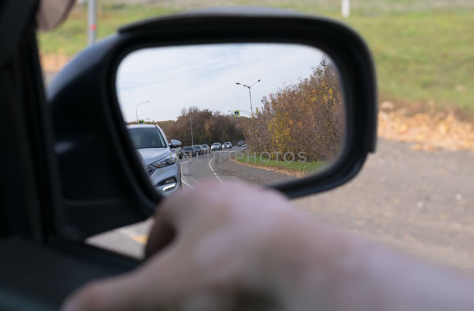 Hand man lying on the car door with a view from the window and with a view of the cars queue in the rear view mirror