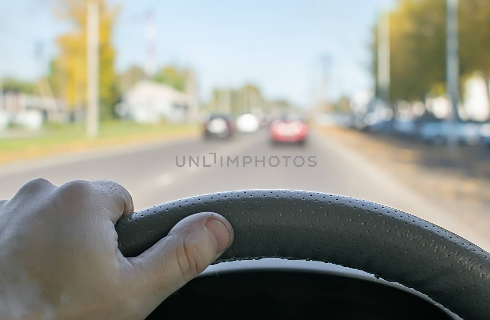 the driver hand on the steering wheel of a car that is passing on a country highway
