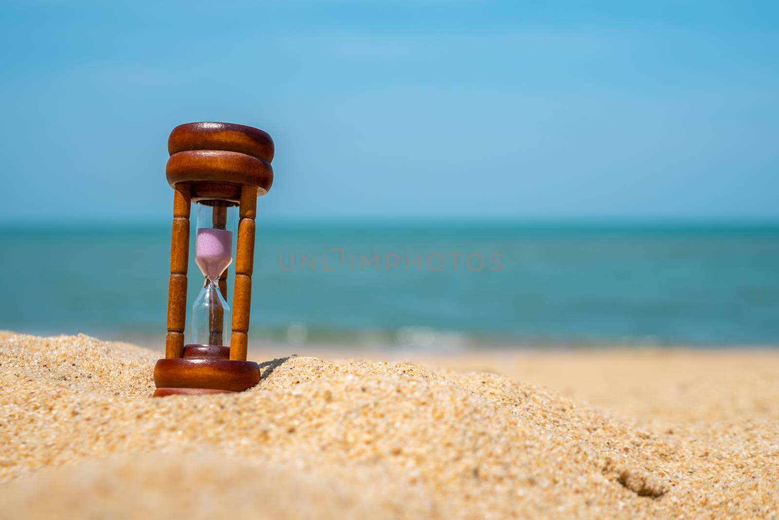 Small hourglass show time is flowing on sand beach texture background.