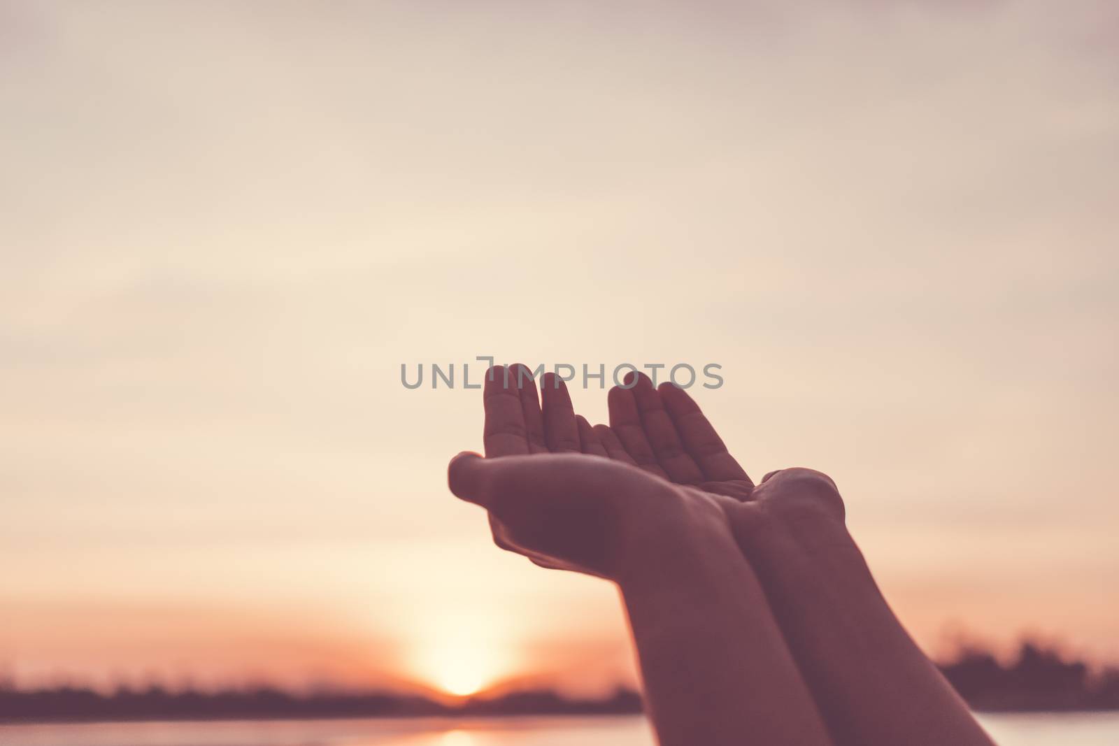 Woman hands place together like praying in front of nature blur beach sunset sky background.