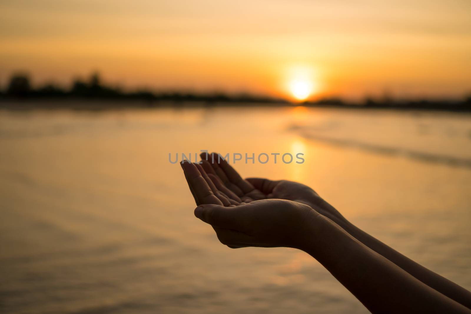 Woman hands place together like praying in front of nature blur beach sunset sky background.