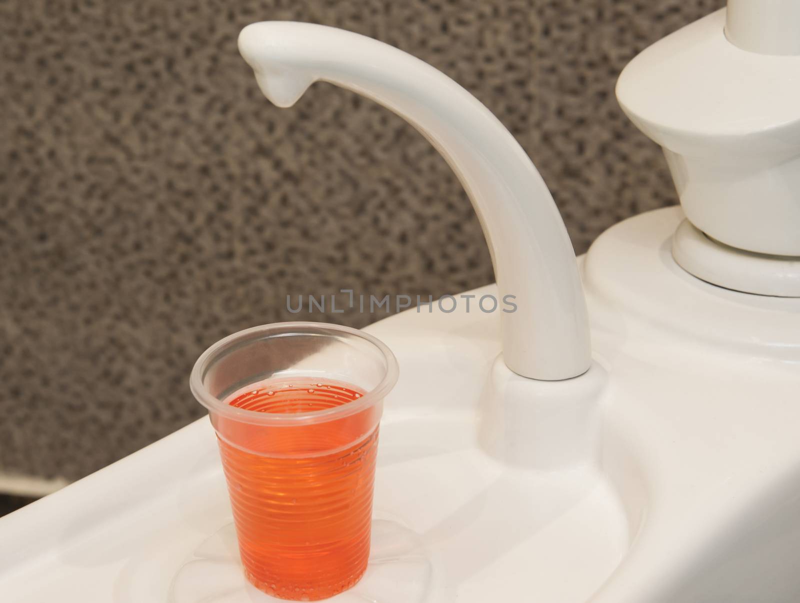 Closeup detail of orange mouthwash drink and faucet in dentists surgery