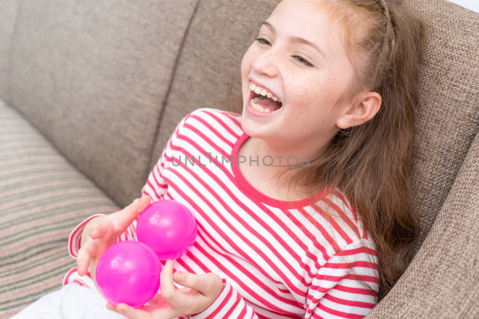 Little girl is laughing and playing with toy on sofa