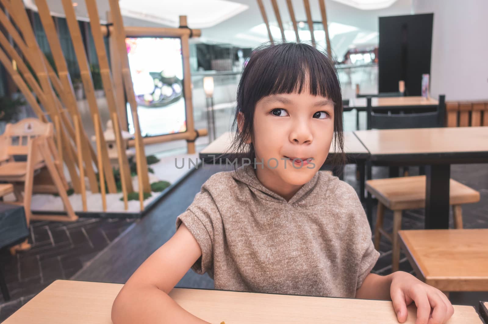 Hungry Funny child licking her lip waiting for food in restaurant.