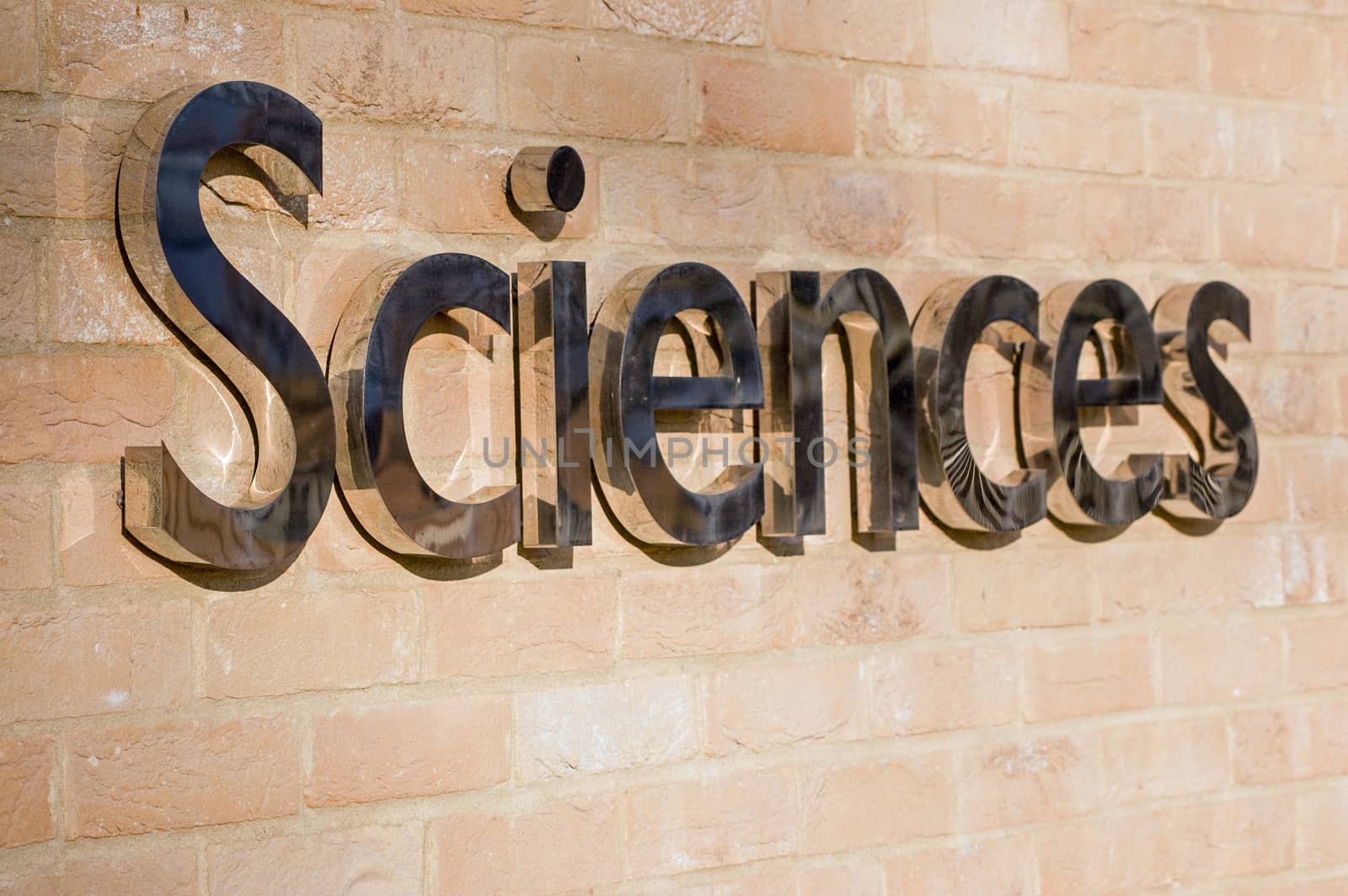 View from an angled perspective of a shiny metal sign outside a university Science building.