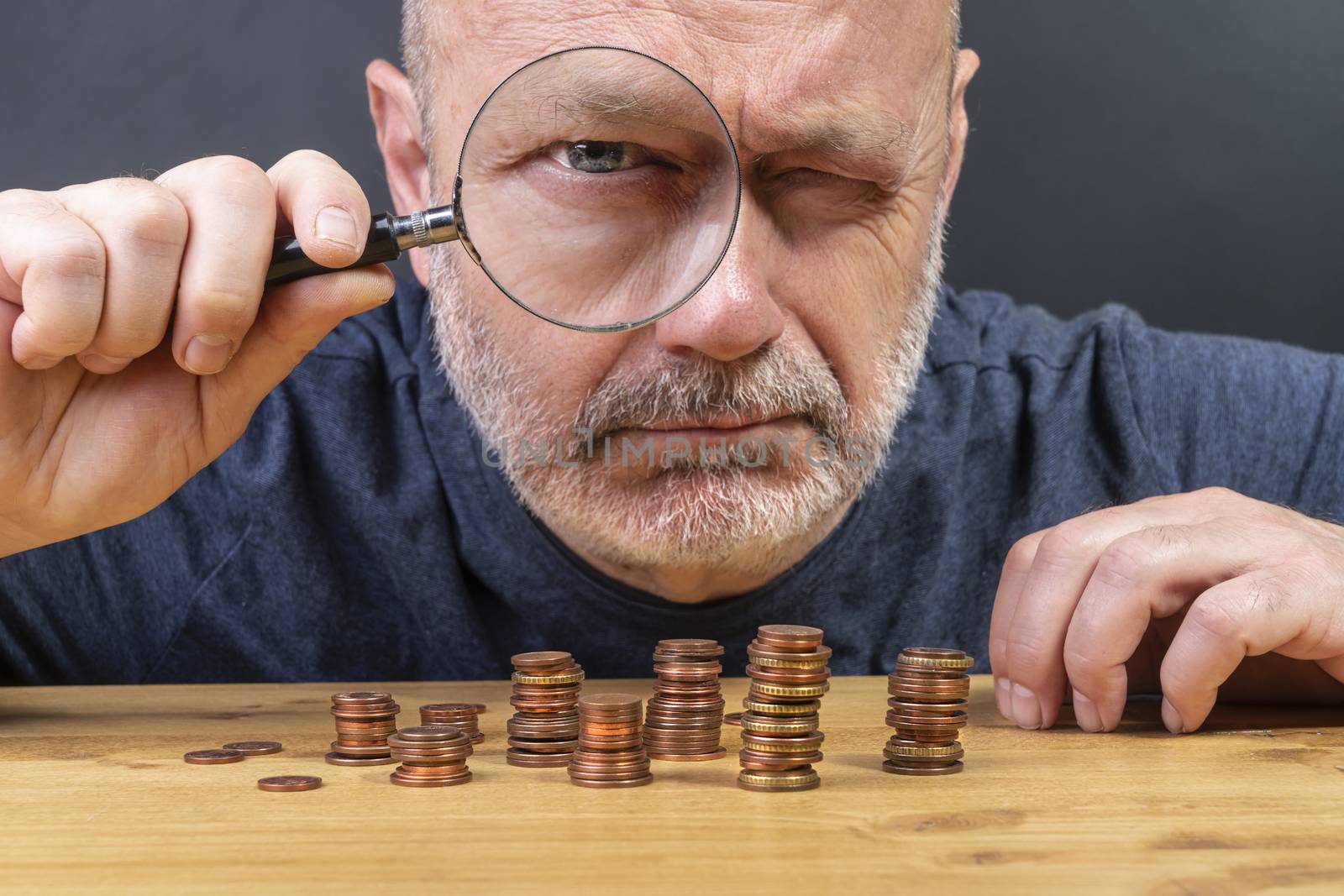 a man with a magnifying glass while counting in coins on a table in a time of crisis