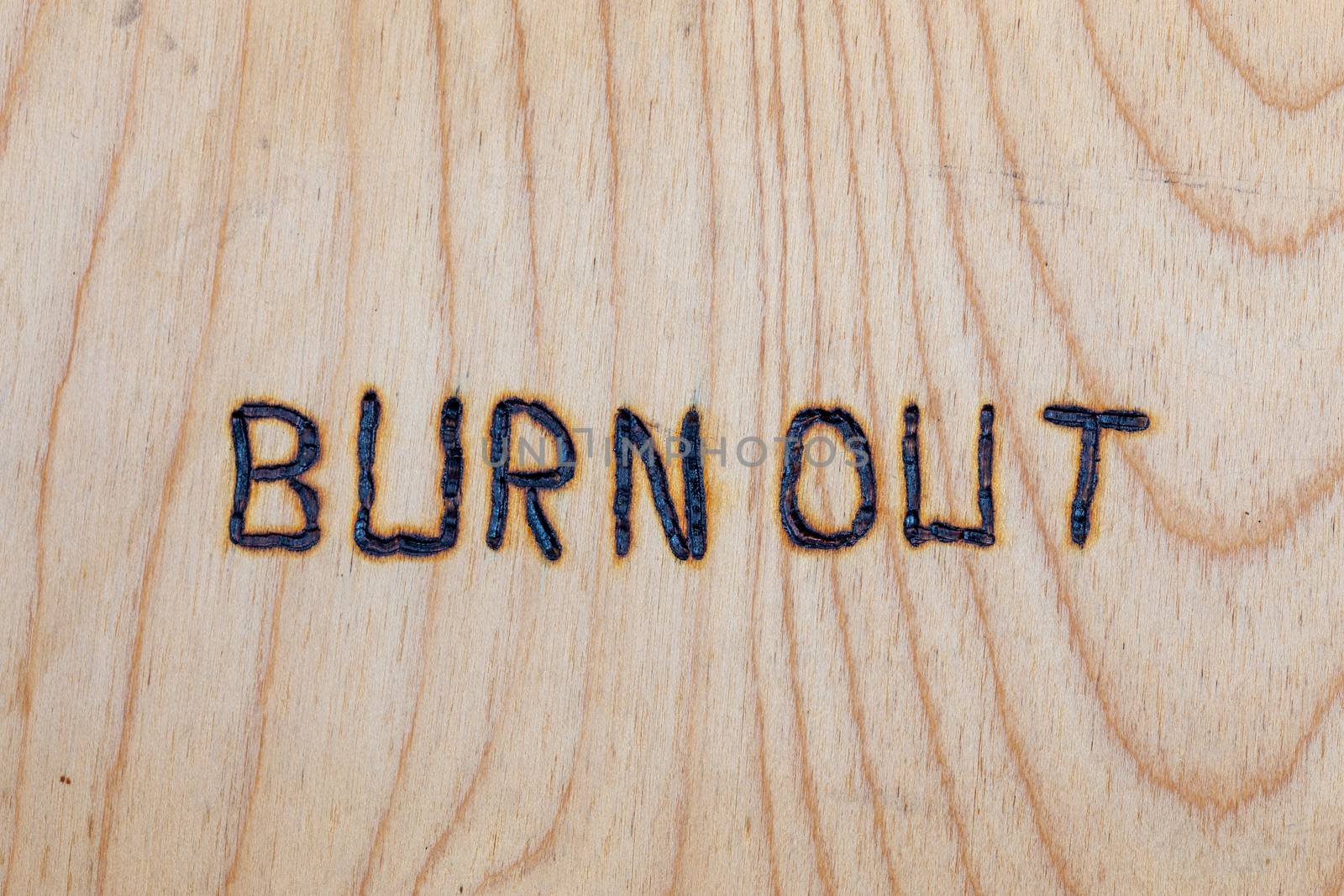 the words burn out handwritten with woodburner on flat plywood surface.