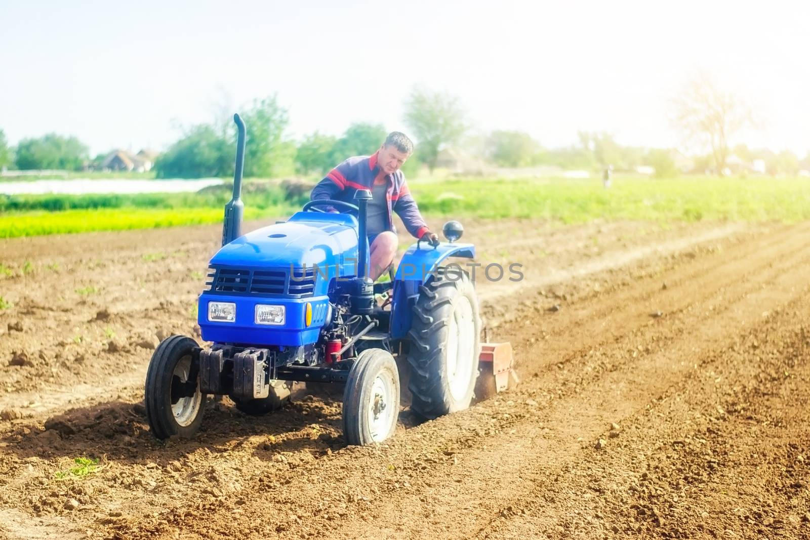 A farmer on a tractor cultivates a farm field. Agriculture, growing organic food vegetables. Soil milling, crumbling and mixing. Loosening the surface, cultivating the land for further planting.