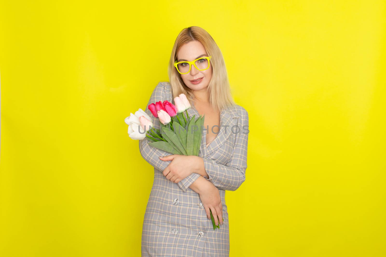 Blonde woman in plaid dress holding tulips bouquet over yellow background