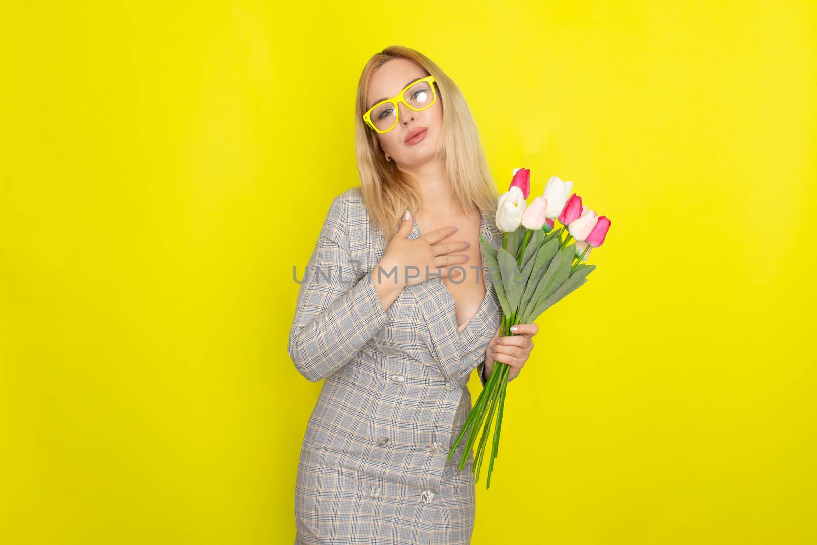 Blonde woman in plaid dress holding tulips bouquet over yellow background