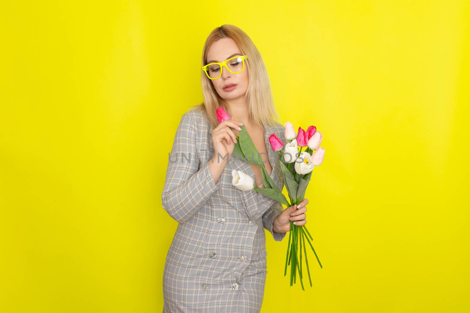 Blonde woman in plaid dress holding tulips bouquet over yellow background