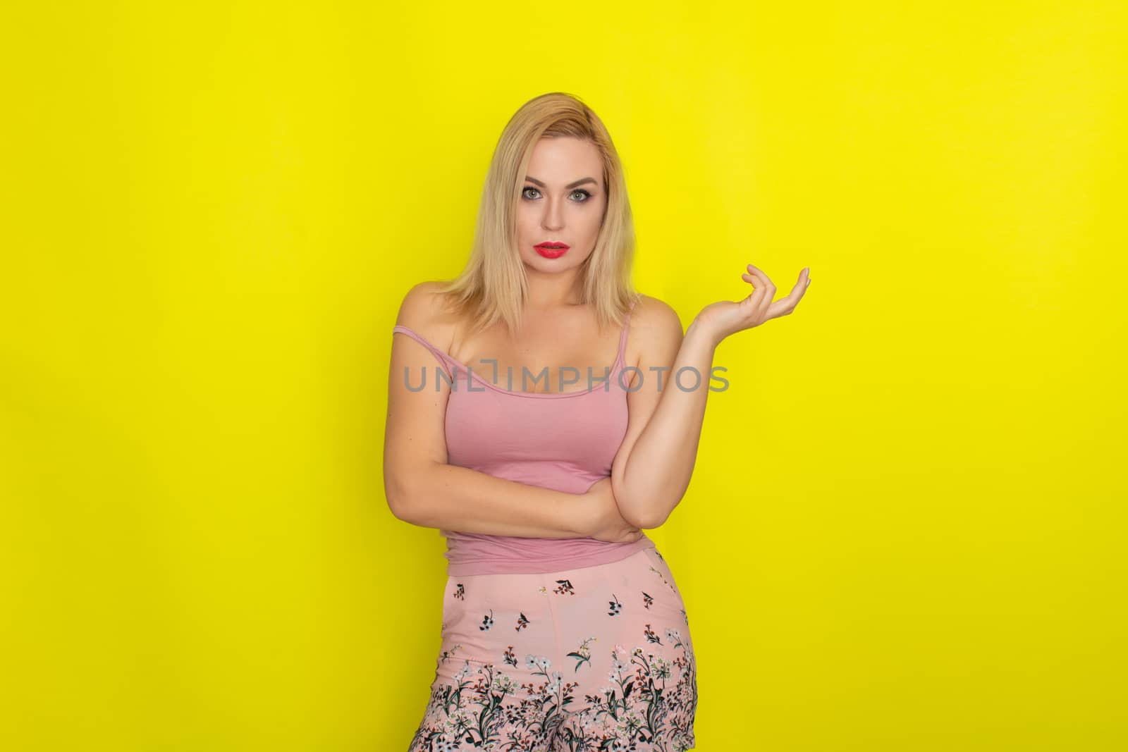 Indoor summer closeup portrait of young stylish fashion glamorous blonde woman posing in pink shorts and shirt, standing over yellow background