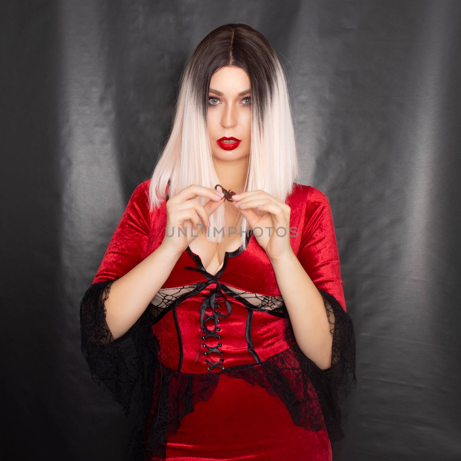 Young beautiful blonde woman in a red vampire dress and with a scorpion on her body in the studio