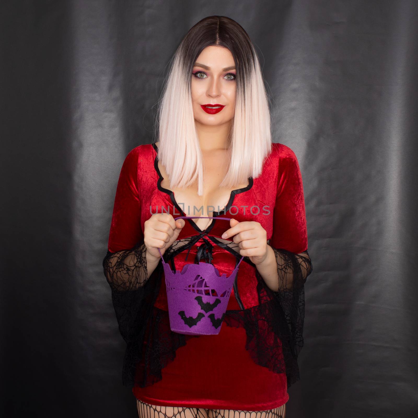 Young beautiful blonde woman in a red vampire dress holds a Halloween purple bag with bats for sweets
