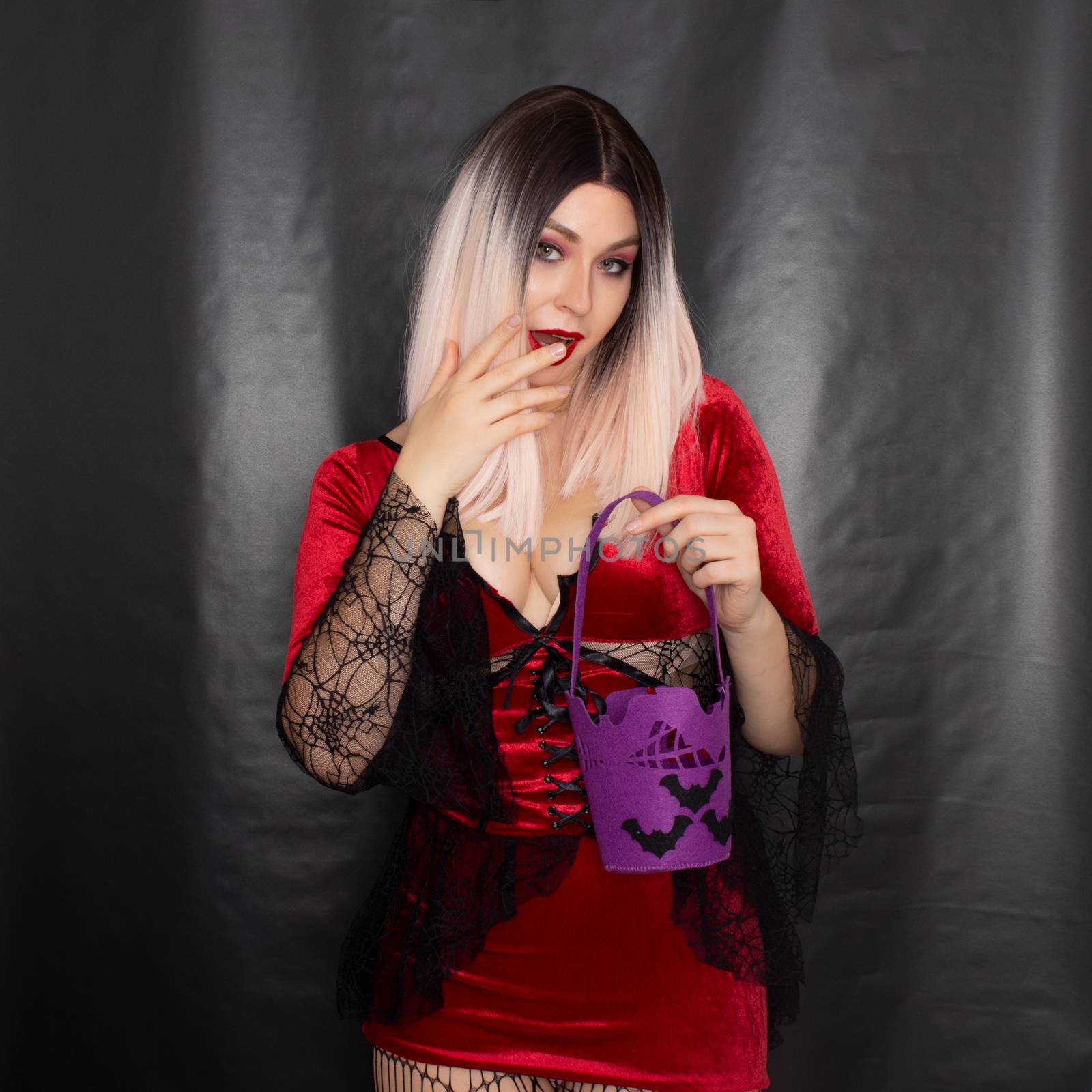 Young beautiful blonde woman in a red vampire dress holds a Halloween purple bag with bats for sweets