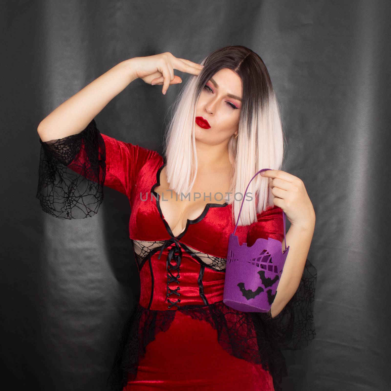 Young beautiful blonde woman in a red vampire dress holds a Halloween purple bag with bats for sweets