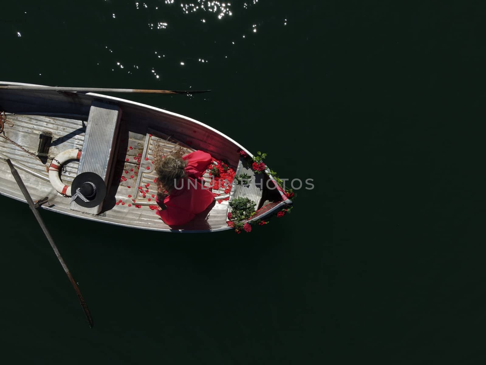 woman with long blond hair on boat with roses and flowers on blue lake