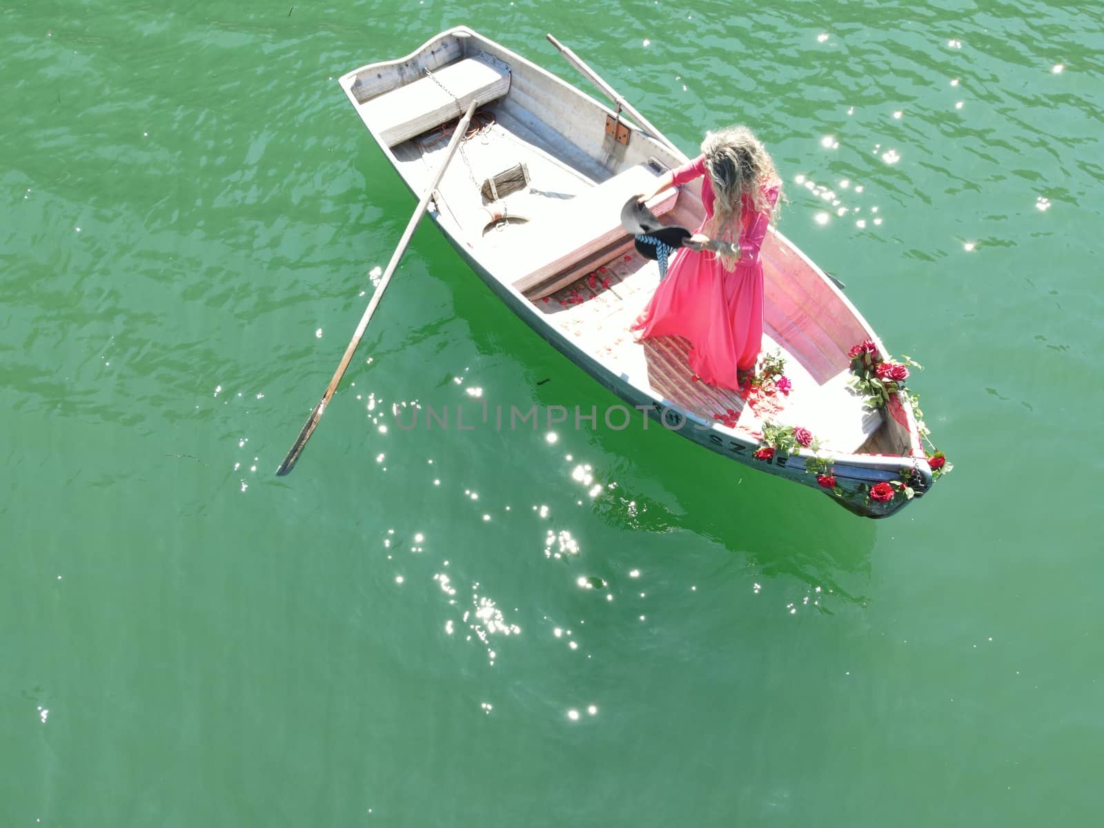 woman with long blond hair on boat with roses and flowers on blue lake
