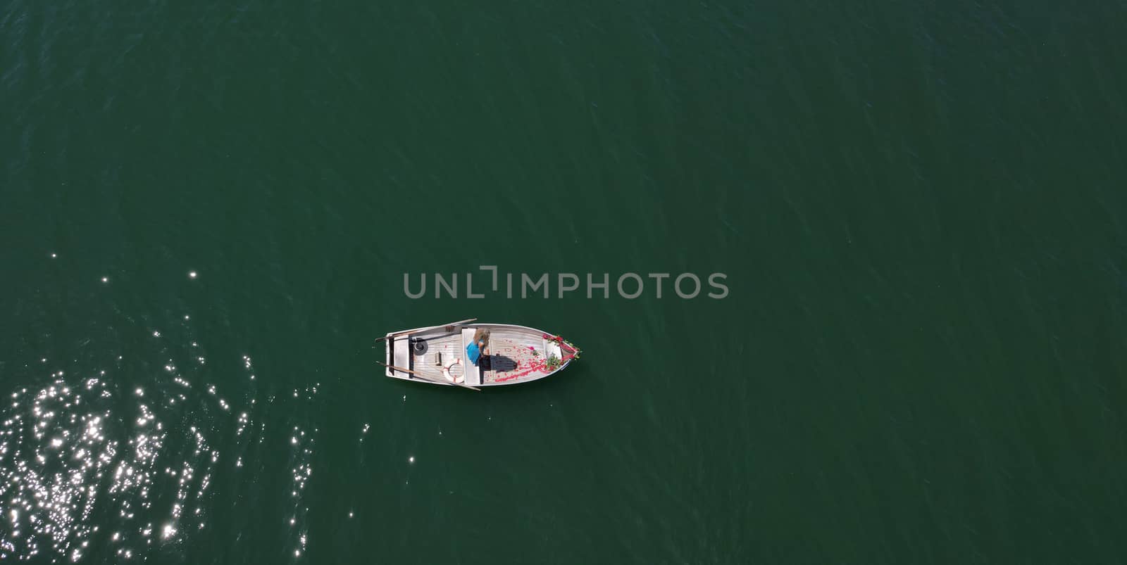 woman with long blond hair on boat with roses and flowers on blue lake