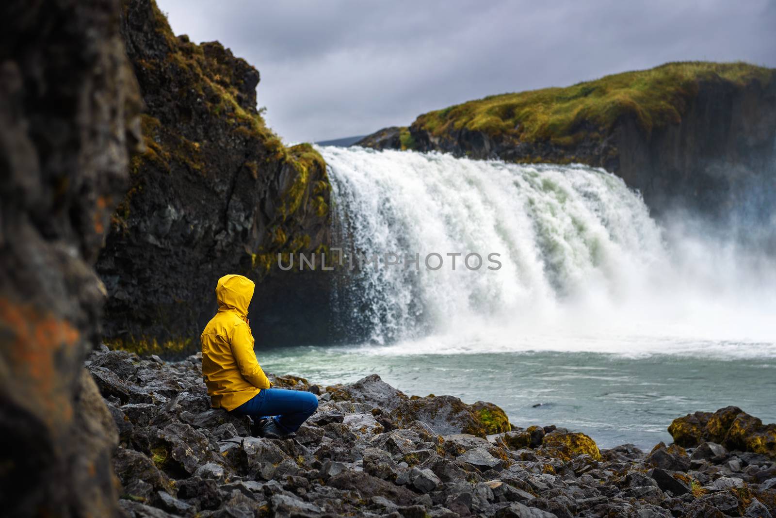 Tourist in a yellow jacket relaxing at the Godafoss waterfall in Iceland by nickfox