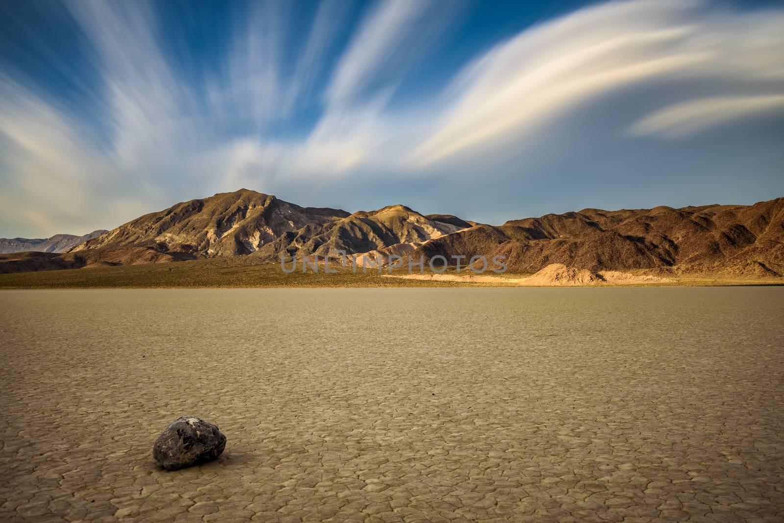 Sailing stone on the The Racetrack Playa in Death Valley National Park during golden hour. The Racetrack Playa is a scenic dry lake with moving stones that inscribe linear imprints. Long exposure.