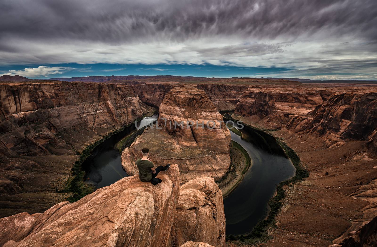 Horseshoe Bend, Colorado river and a hiker sitting at the edge and enjoying the panoramic view.