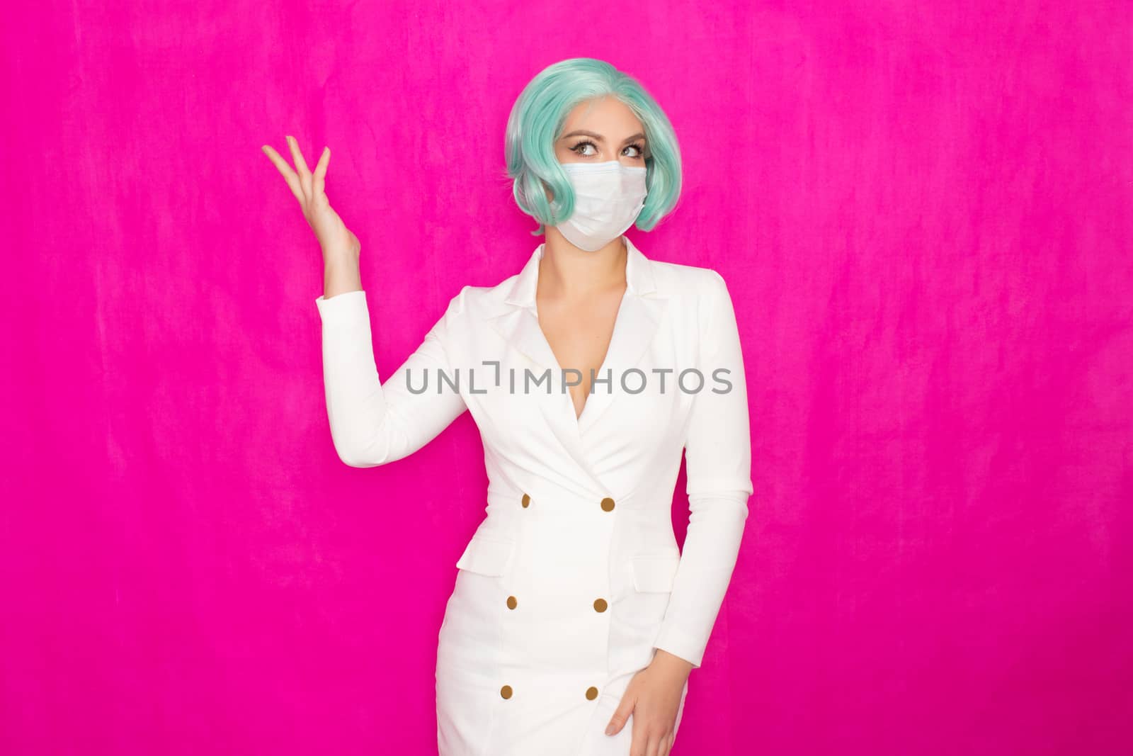 Beautiful young woman with short blue hair in a white business dress jacket with a medical mask posing on a pink background in the studio