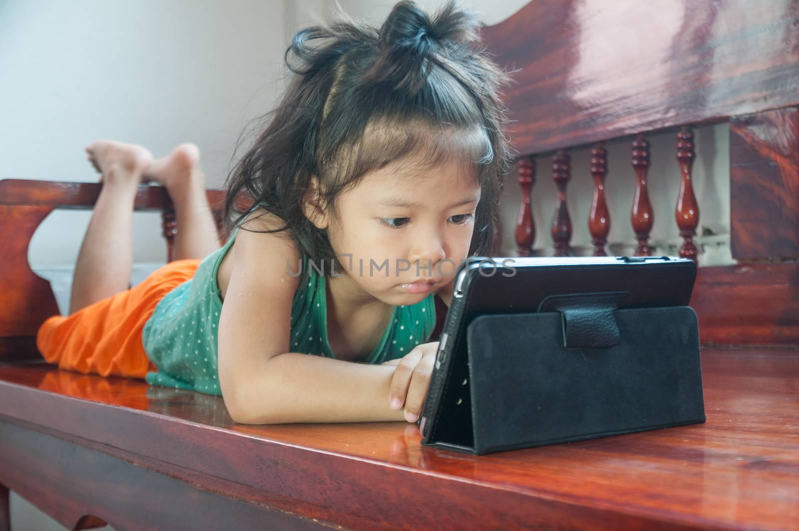 Young Girl lying on wooden stool and Learning online course on Wireless Digital Tablet while staying at home in situation of Corona Virus or Covid 19 outbreak.