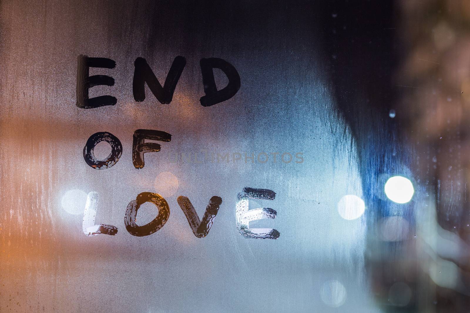 the words end of love handwritten on night wet window glass, closeup with selective focus and bokeh blur