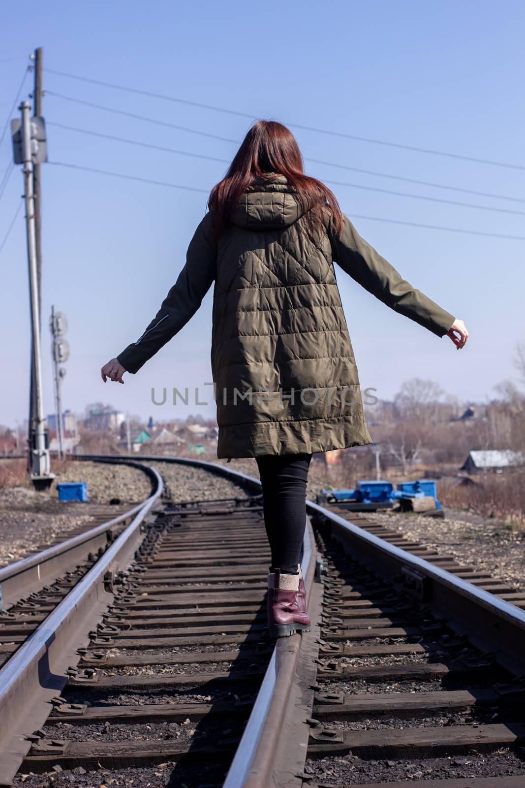 The girl is walking on the railway in front. Rear view