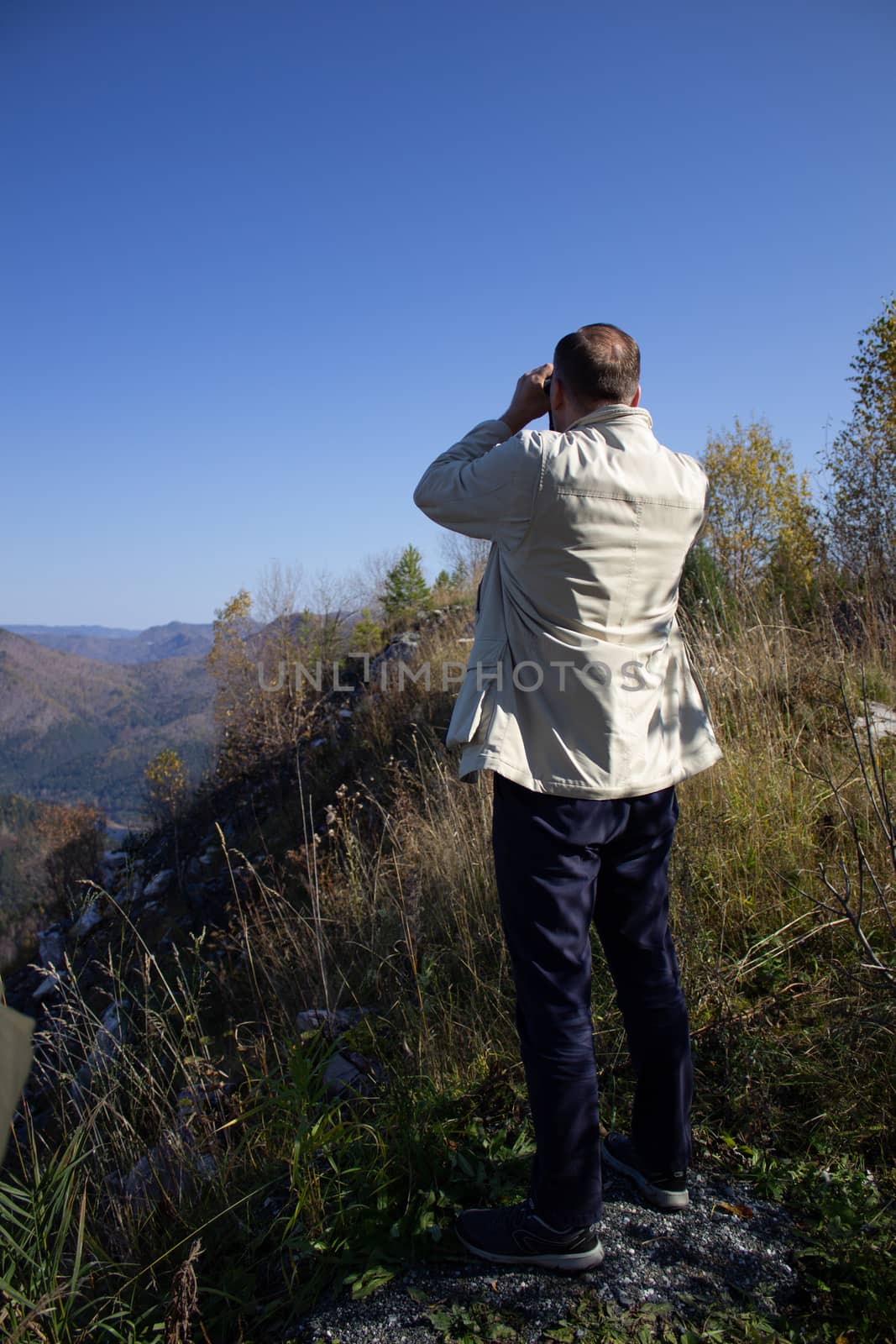Mountaineer looking through field glasses while standing on a mountain peak