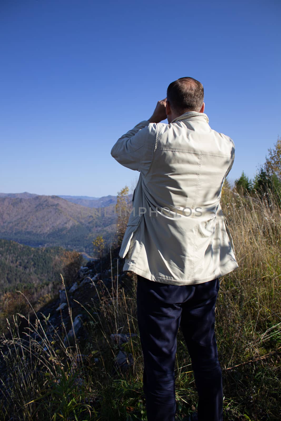 Man look through binoculars into the mountains by AnatoliiFoto
