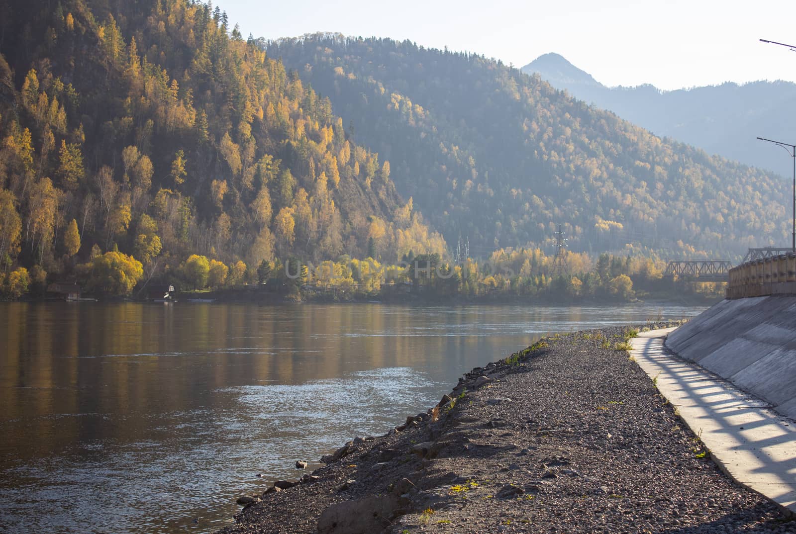 A wide river that lies in the mountain valley. Mountains near the river are covered with forests.