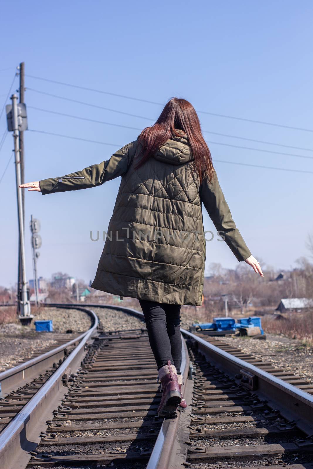 The girl is walking on the railway in front. Rear view