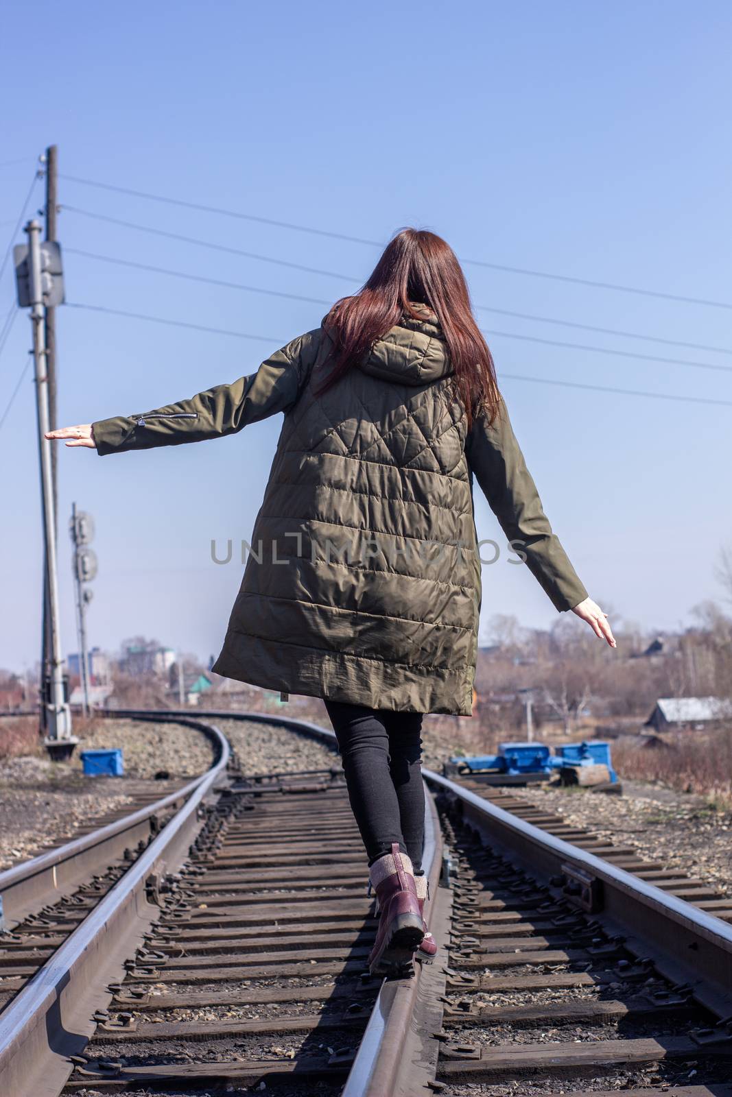 The girl is walking on the railway in front. Rear view. by AnatoliiFoto