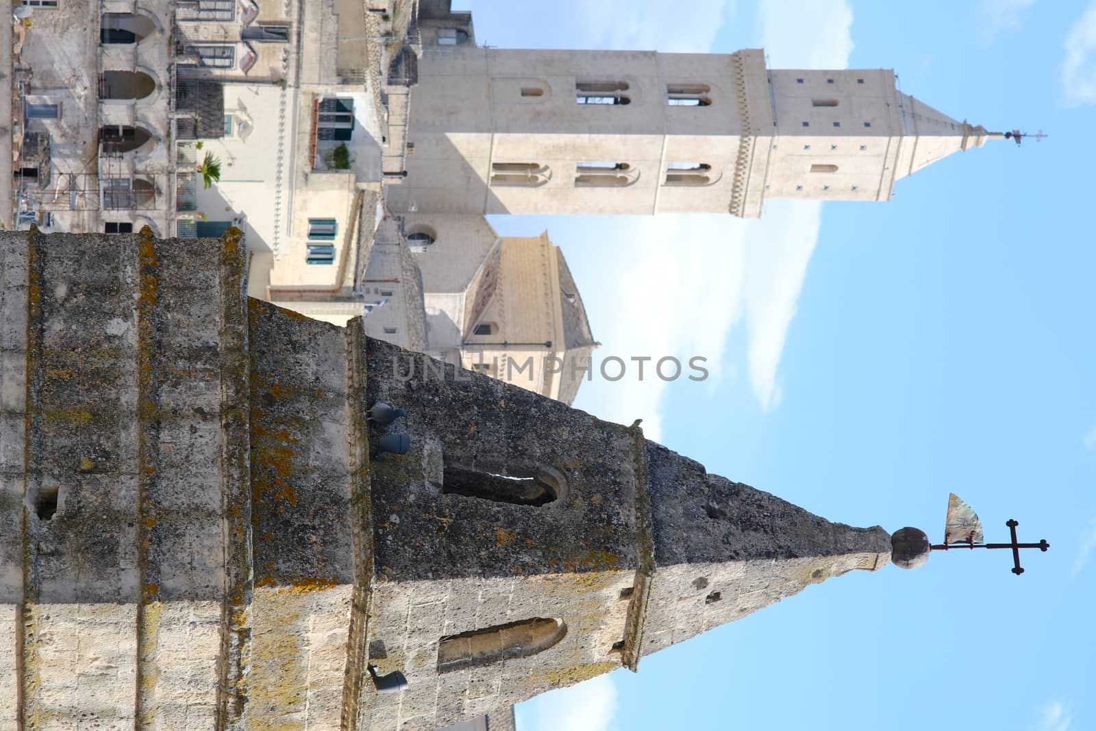 Point of two bell towers and church in the ancient city of Matera in Italy. Construction with blocks of tufa stone. Chileo blue with clouds.