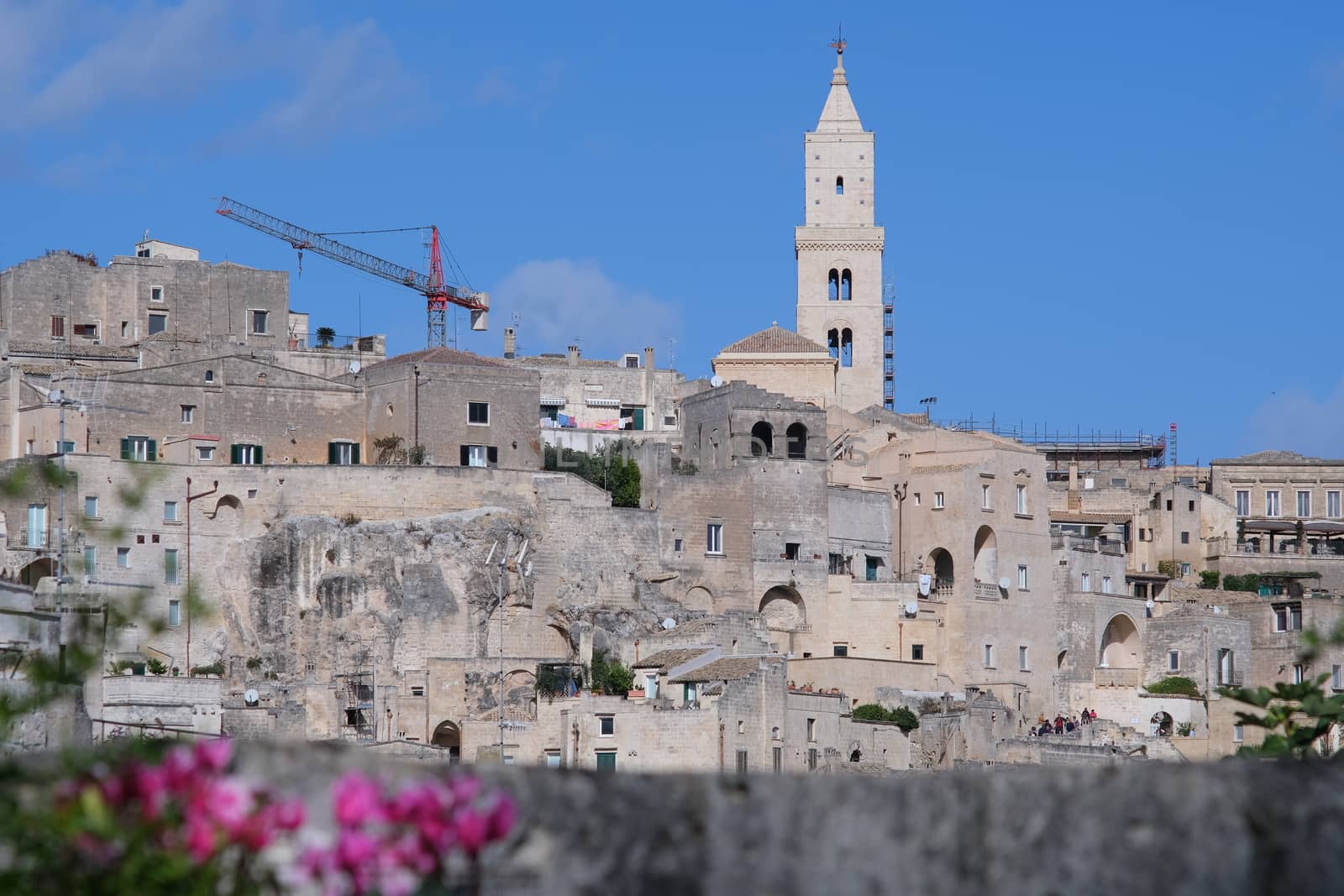 Panorama of houses and of the Sassi of Matera with roofs and streets. Blue sky with church and bell tower with blue sky background with clouds.