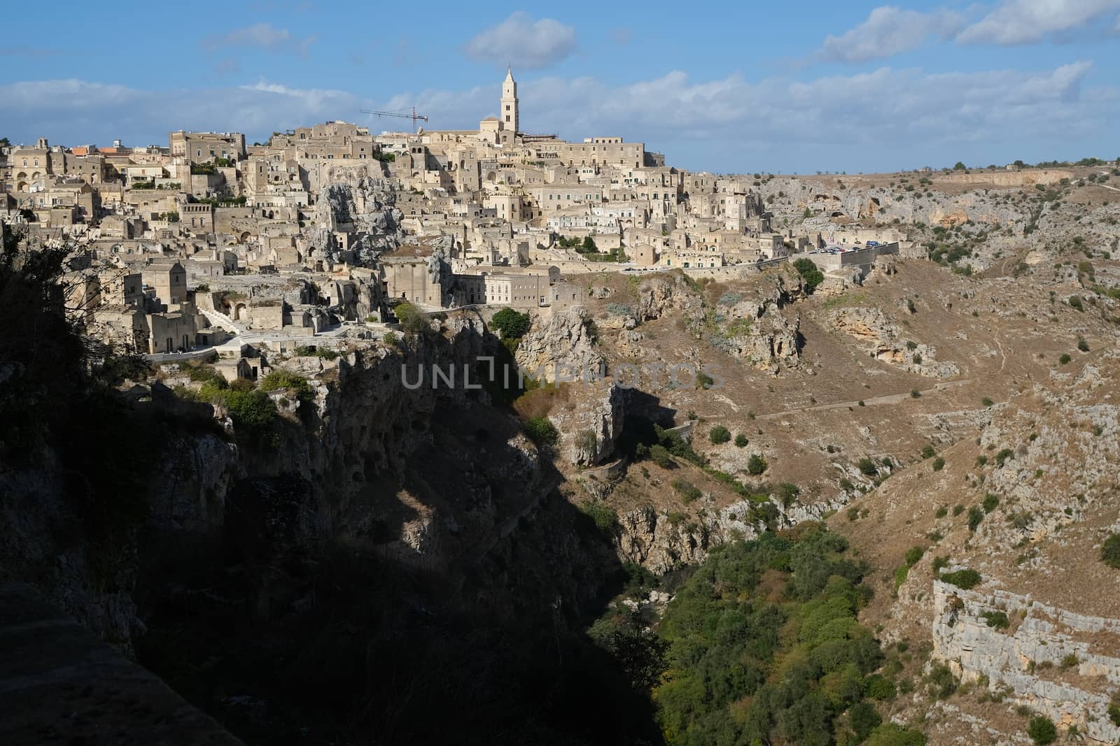 Panorama of houses and of the Sassi of Matera with roofs and streets. Blue sky with church and bell tower with blue sky background with clouds.