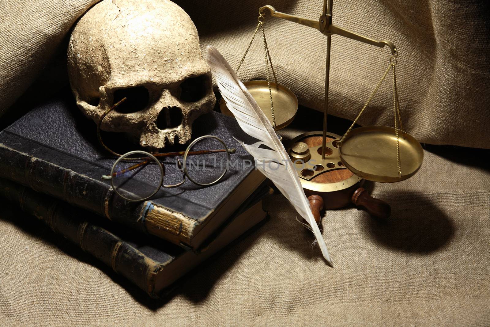 Old books and quill pen near human skull on canvas background