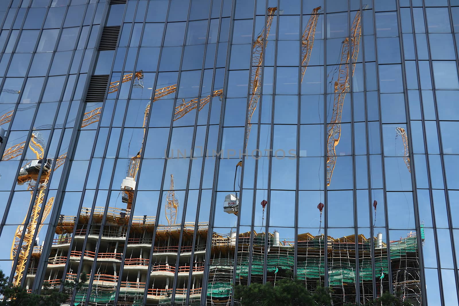 Glass facade of a building with reflection of a construction site. Cranes and scaffolding