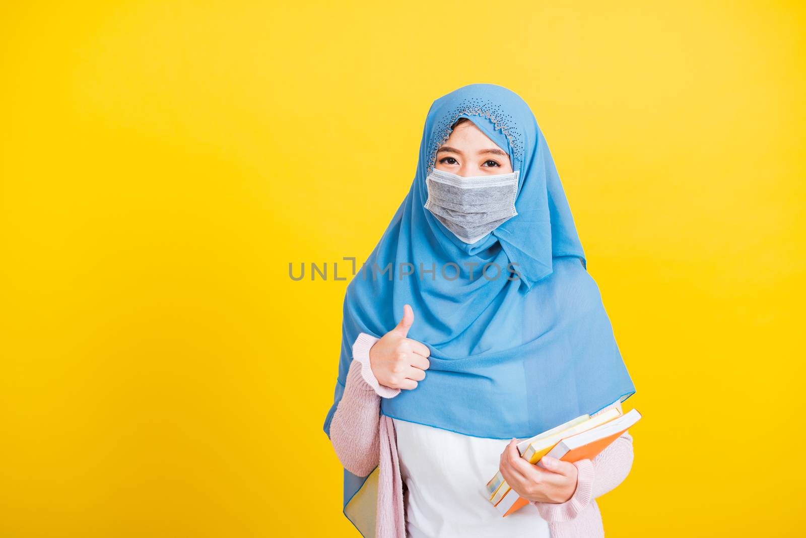 Asian Muslim Arab, Portrait of beautiful young woman religious wear veil hijab and face mask protective to prevent coronavirus hold books on hand and show finger thumb up for good sign Back to college