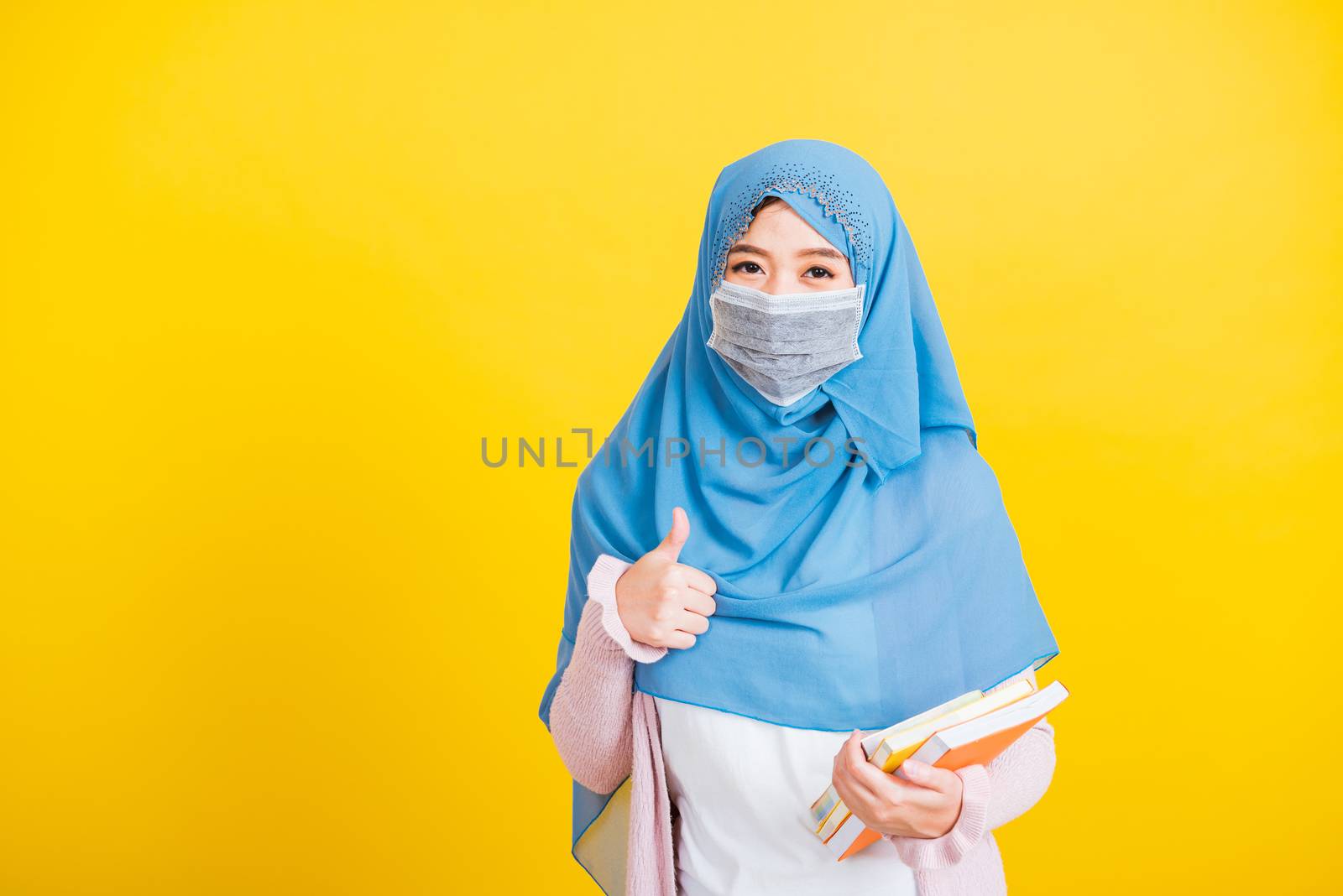 Woman wear hijab and face mask protective hold books on hand and by Sorapop