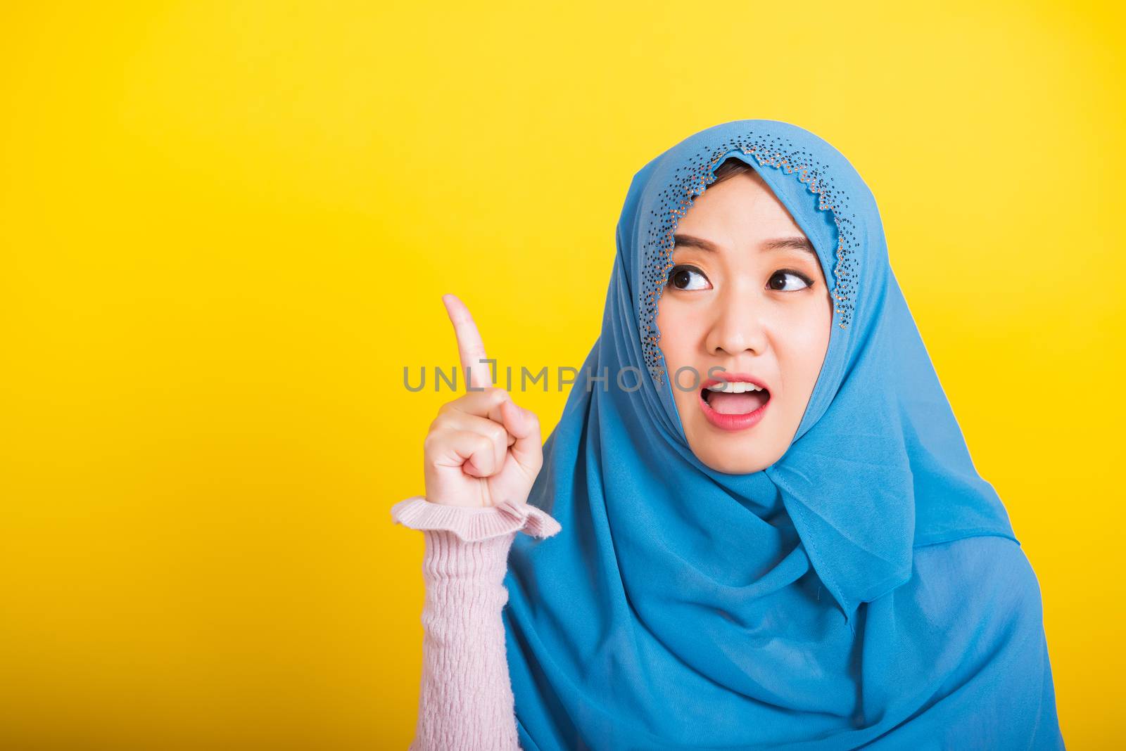 Asian Muslim Arab, Portrait of happy beautiful young woman Islam religious wear veil hijab funny smile she positive expression pointing with finger up to space isolated yellow background