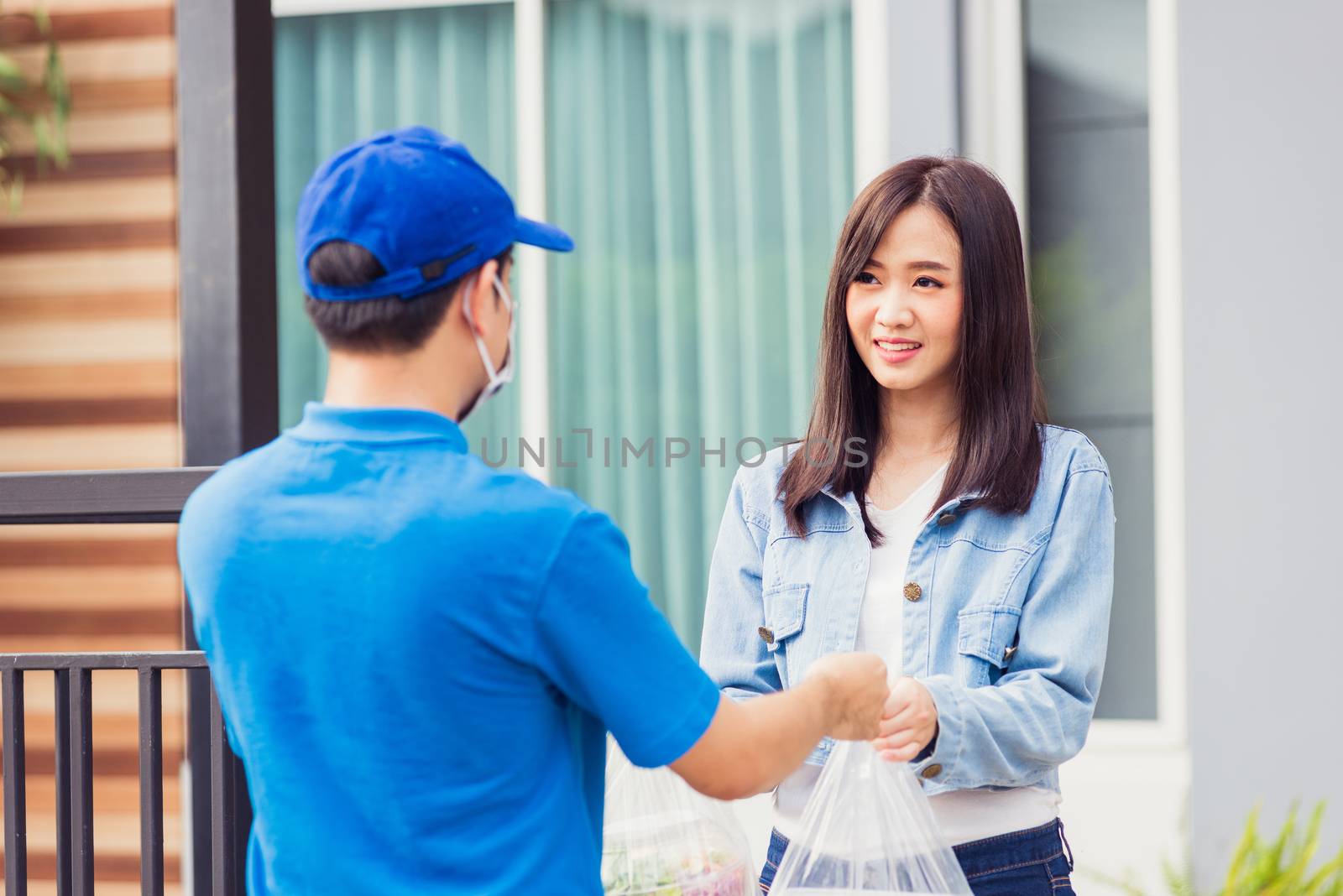 Asian young delivery man wear face mask he making grocery service giving rice food boxes plastic bags to woman customer receiving door at house after pandemic coronavirus, Back to new normal concept