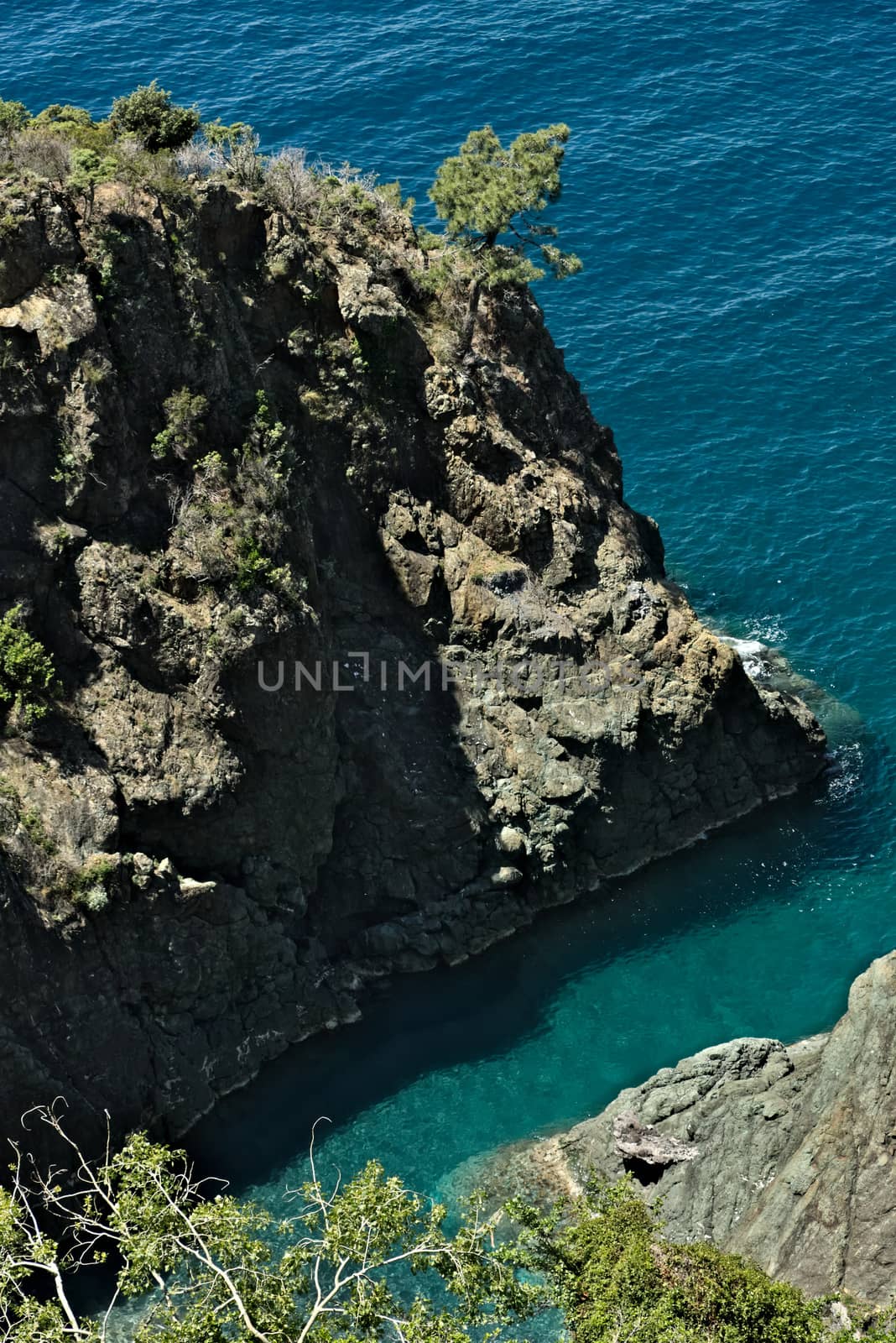 Sea waves break on the rocks of the Ligurian mountain.  Near the Cinque Terre a seascape with blue sea and dark red rocks. Village of Framura.