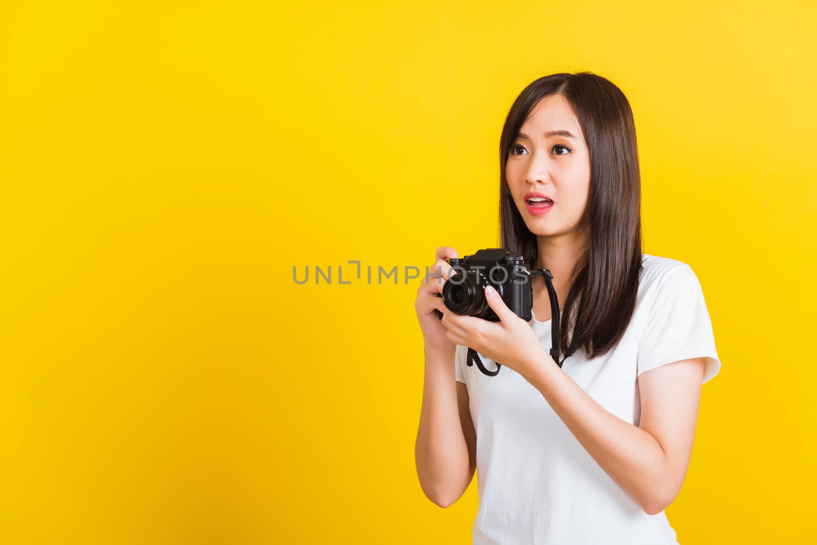 Portrait of happy Asian beautiful young woman photographer holding vintage digital mirrorless photo camera on hands, studio shot isolated on yellow background, lifestyle teenager hobby travel concept