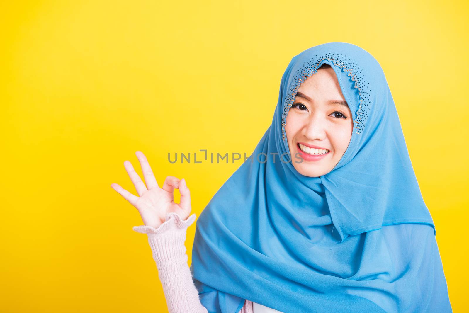 Asian Muslim Arab, Portrait of happy beautiful young woman Islam religious wear veil hijab funny smile she showing gesture fingers in okay gesture symbol, OK sign isolated yellow background