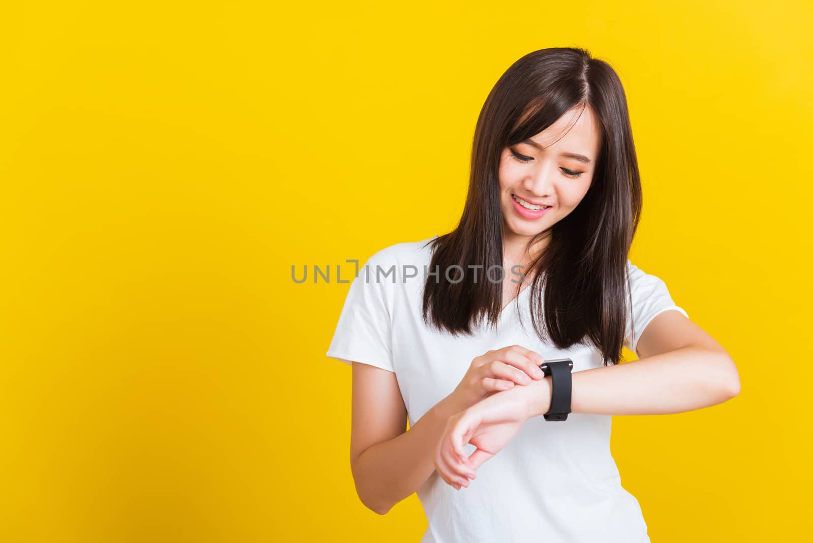 Portrait Asian of a happy beautiful young woman smiling looking and pointing finger her smart wristwatch studio shot isolated on yellow background